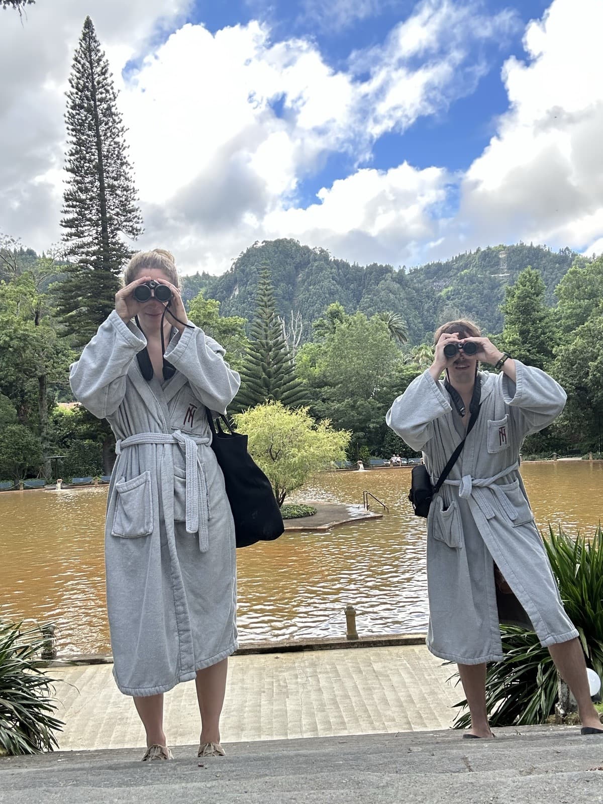 Jen and Luke in matching robes birding with binoculars by a lake